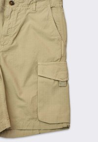 Pantaloni cargo beige realizzati in tessuto leggero, con chiusura a bottone, tasche laterali e una grande tasca cargo sulla coscia.