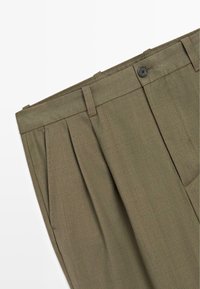 Pleated olive green trousers with a textured fabric, featuring a black button closure and side pockets.