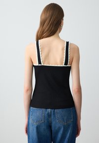Top nero a costine con rifiniture bianche a onda su spalline e scollatura, abbinato a jeans in denim azzurro chiaro a vita alta.