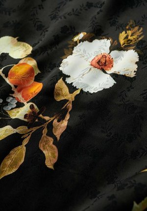 Tessuto nero con stampe floreali in sfumature di bianco, arancione e verde. Include intricati motivi fogliari e dettagli di texture sottili.
