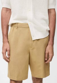 Beige bomullsshorts med knäppning och bälteshällor, med sidofickor och rak passform, parat med en strukturerad vit trikåtröja.