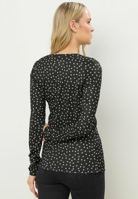 Langsleeve top in zwarte stof met witte stippen. Heeft een ronde halslijn en een getailleerde silhouette. Soepele textuur.