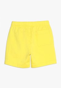 Žluté bavlněné šortky s elastickým pasem, mají zadní kapsu a volný střih. Hladká textura a jednoduchý design.