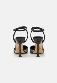 Sandali neri con tacco alto e cinturini alla caviglia, con tomaia testurizzata decorata con strass trasparenti sul tacco e sui lati.