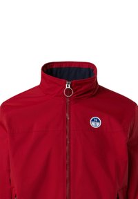 Giacca impermeabile rossa con colletto alto, chiusura a zip argento e logo blu circolare sul lato sinistro del petto. Texture liscia, design informale.
