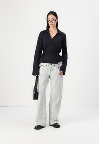 Black wrap shirt with a tie detail, paired with light gray striped wide-leg jeans. Accessories include a black bag and round glasses.