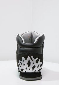 Bota negra con una parte superior de cuero liso y ante, que presenta un gráfico plateado texturizado en el talón y un interior blanco acolchado.