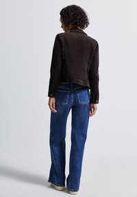 Veste en velours côtelé marron avec un col, jeans bleus évasés et baskets beiges. Détails de couture visibles et poches sur les deux vêtements.