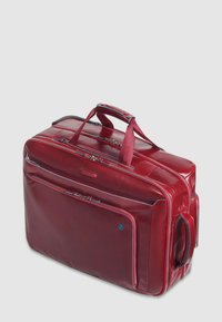 Bolso de cuero rojo tipo duffel con dos asas superiores, un bolsillo frontal con cremallera y detalles en azul en las cremalleras. Diseño rectangular y elegante con textura brillante.