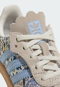 Baskets Adidas Samba avec un motif floral multicolore. Comprend du daim beige, des rayures bleues et une languette festonnée. Lacets blancs et semelle en caoutchouc.
