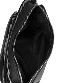 Czarna skórzana torba z srebrnym zamkiem. Wnętrze wyłożone czarnym materiałem, ukazujące otwartą przestrzeń bez dodatkowych przegródek czy kieszeni.
