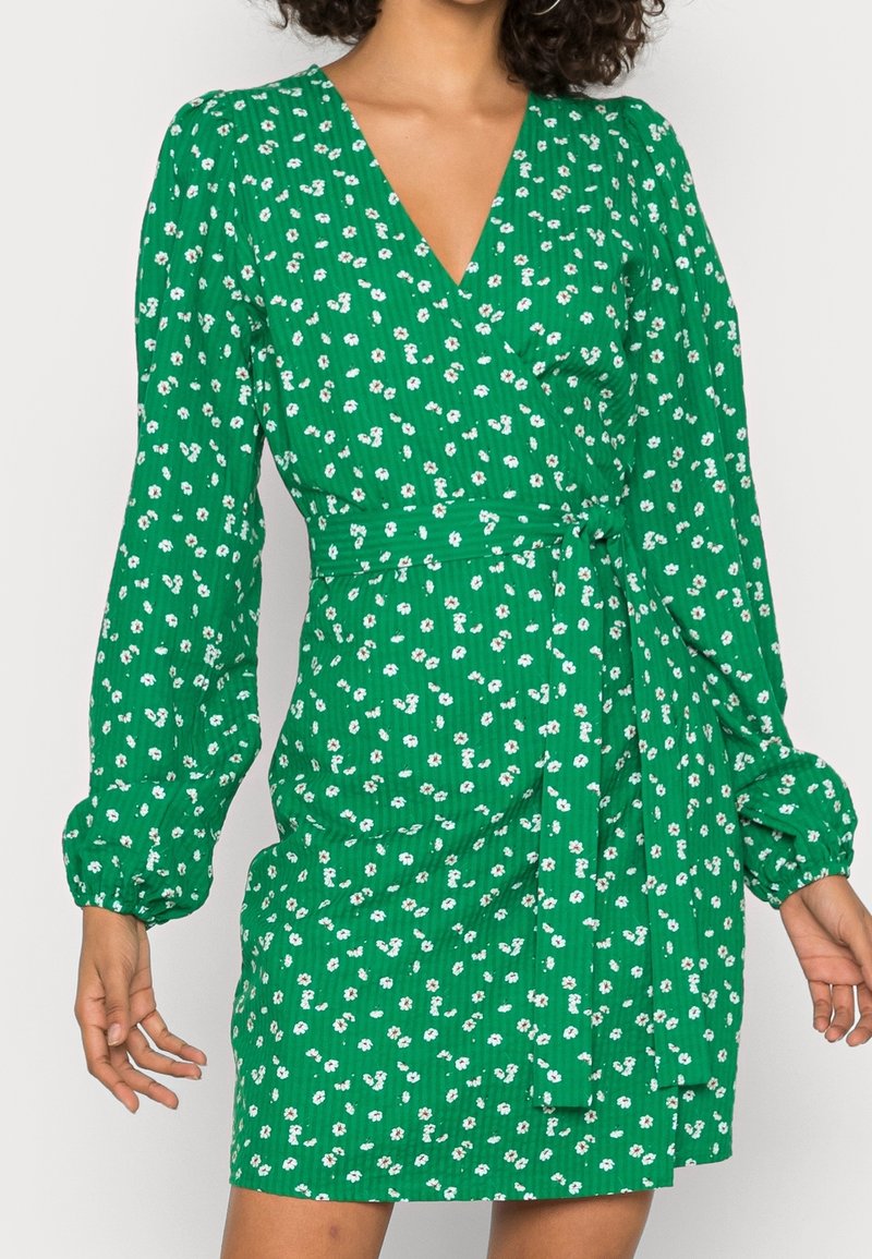 Vestido verde floral con escote en V y largas mangas abullonadas. Presenta un cinturón atado en la cintura y una tela texturizada con pequeñas flores blancas.