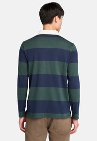 Playera de polo de manga larga con rayas horizontales en azul marino y verde, con un cuello blanco y un ajuste relajado, fabricada en una suave tela texturizada.