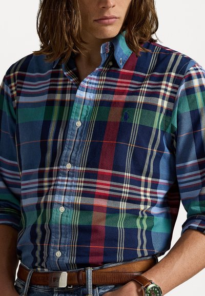 Daugiaspalvė languota marškiniai su įvairiomis mėlynomis, žaliomis ir raudonomis atspalviais, mygtukų kaklas ir mažas logotipas ant krūtinės. Textūruotas medvilninis audinys.