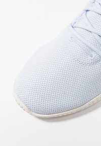 Ljusblå mesh-sneakers med en texturerad yta, med rund tå och en vit gummisula. Snörena är tydligt synliga.