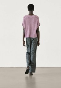 Vaaleanpunainen neulepaita lyhythihaisilla hihoilla ja ribbaamalla, yhdistettynä tummiin raidallisiin leveälahkeisiin housuihin, nähtynä takaa.