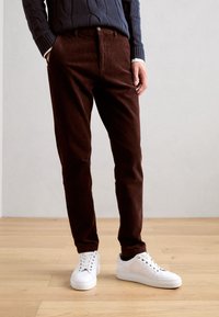 Bruna kordbyxor med slim fit, tillsammans med vita sneakers. Byxorna har sidofickor och en subtil textur. Tröjan är marinblå med en kabelstickad design.