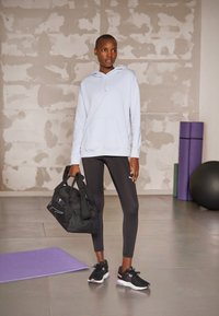 Felpa con cappuccio azzurro chiaro, tasca frontale, leggins neri, scarpe da ginnastica nere con dettagli rosa e una borsa da palestra nera. Materassino da yoga viola sullo sfondo.