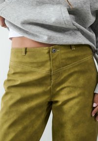 Zielone oliwkowe spodnie z ekoskóry o gładkiej fakturze, z kontrastowym białym przeszyciem i zapięciem na guzik w talii.