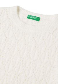Weißer Strickpullover mit einem strukturierten Rautenmuster und einem gerippten Rundhalsausschnitt. Das Etikett trägt "UNITED COLORS OF BENETTON" in grüner Schrift.