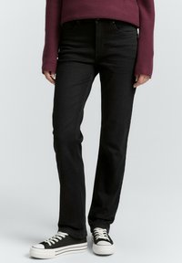 Černé džíny s rovnými nohavicemi vyrobené z denimu, s klasickým pětipocket designem. V kombinaci s vínovým žebrovaným svetrem a černými teniskami.