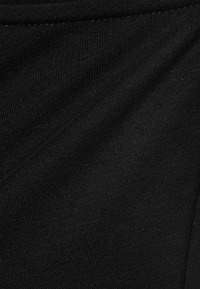Gros plan sur un tissu tricoté côtelé noir montrant la texture et les détails fins des coutures horizontales.