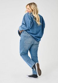 Chemise oversized en denim bleu clair avec épaules tombantes, assortie à un jean droit bleu clair et des baskets montantes noires.