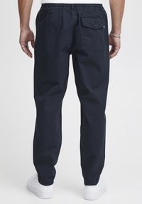 Mörkblå cargobyxor med elastisk midja, med en bakficka med klaffstängning. Slät tygkvalitet och smal passform. Vita sneakers synliga.