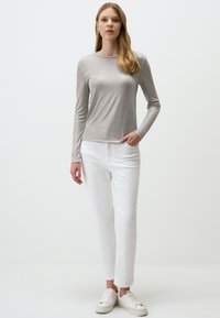 Langärmeliges, hellgraues Oberteil aus einem glatten Material. Kombiniert mit weißen, geraden Hosen und weißen Sneakers. Minimalistisches Design.