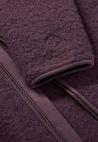 Fleece-takk in djup lila, med en mjuk textur, dragkedjestängning, ribbade muddar och en broderad logodetalj på ärmen.