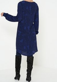 Navy blue long-sleeve dress with a textured pattern, featuring a slight V-back design, paired with knee-high black suede boots.