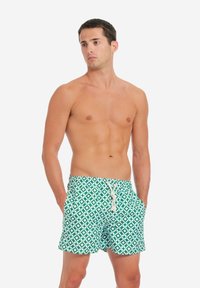 Pantaloni da bagno verdi realizzati in un tessuto con un motivo geometrico bianco. Presentano una vita elastica con dettaglio di cordoncino.