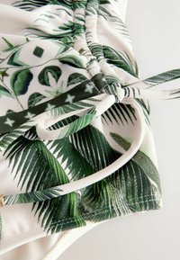 Vitt badkläder med ett grönt tropiskt bladmönster, justerbar knytning och rynkat tyg för en texturerad look.