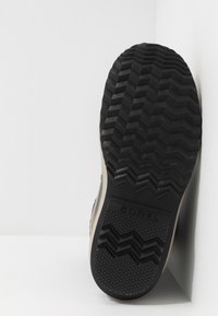 Suela de goma negra con un patrón de tracción en zigzag, con un lado beige. Logo "SOREL" grabado en la suela, visto desde un ligero ángulo.