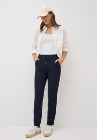 Marine joggers met elastische tailleband, trekkoord en zijzakken. Gecombineerd met een witte tanktop en een lichtblauw overhemd, afgerond met witte sneakers.