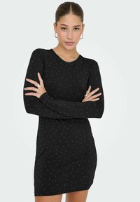 Svart klänning med långa ärmar, figursydd design och utspridda vita prickmönster. Mjuk tyg med rund halsringning och minimal detaljering.