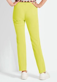 Limettengrüne Slim-Fit-Hosen mit glatter Textur, ausgestattet mit zwei Gesäßtaschen und geradem Bein-Fit, kombiniert mit weißen Sneakers.