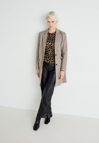 Blazer en laine beige, haut à imprimé léopard, pantalon en cuir noir et bottes noires à bout carré. Tissus texturés, coupe ajustée et design structuré.