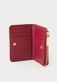 Interno di un portafoglio rosso in pelle con più scomparti per carte, chiusura a scatto, cerniera dorata e logo del marchio impresso; finitura morbida e texturizzata.