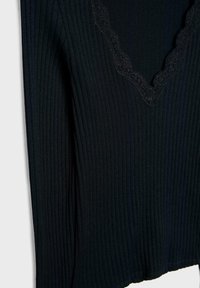 Sort ribbet sweater med V-hals og bølgemønster. Stoffet har en blød tekstur og en tætsiddende pasform.
