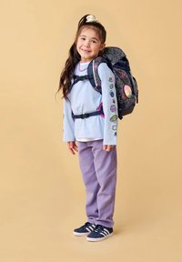 Navy-Rucksack mit einem sternenmuster, lila Hose, hellblaues Langarmshirt mit bunten Designs und dunklen Schuhen mit weißen Streifen.