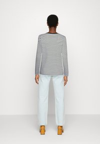 Camisa de mangas longas às riscas em preto e branco, combinada com jeans de cintura alta azul claro e sapatos de salto quadrado castanhos.