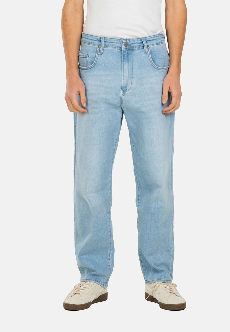 Vaqueros de mezclilla azul claro con corte recto, cinco bolsillos y bragueta de botones, combinados con zapatillas blancas. Textura suave y ligera decoloración.