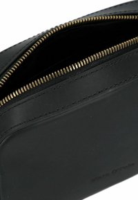 Borsa a zip in pelle nera con una texture liscia, dettagli della cerniera in tono oro e bordi cuciti, caratterizzata da un design rettangolare semplice.