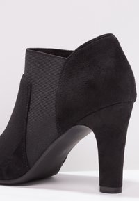 Bottine noire en suède lisse et tissu texturé, avec un talon effilé et un design élégant.