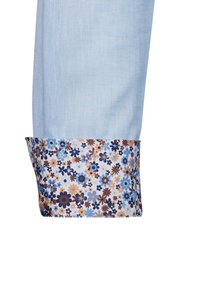 Manica in tessuto azzurro chiaro con polsino a motivo floreale, caratterizzato da fiori blu, marroni e crema su uno sfondo bianco.