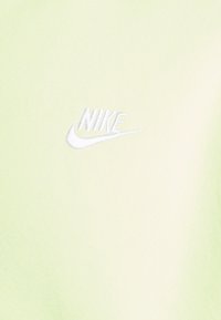 Logo Nike brodé blanc avec swoosh sur un fond en tissu vert clair.