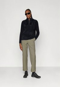 Maglione in pile nero con mezza cerniera, abbinato a pantaloni cargo verde oliva chiaro e sneaker nere. Il materiale sembra morbido e strutturato.