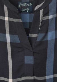 Col de chemise à carreaux bleu marine et gris avec un col en V et une étiquette cousue portant l'inscription "feeling lucky".