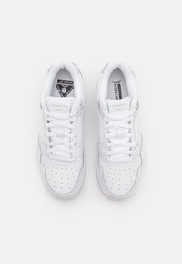 Sapatos desportivos brancos com um design de biqueira perfurada, atacadores planos e amortecimento. Apresenta uma marcação na língua e nos lados.